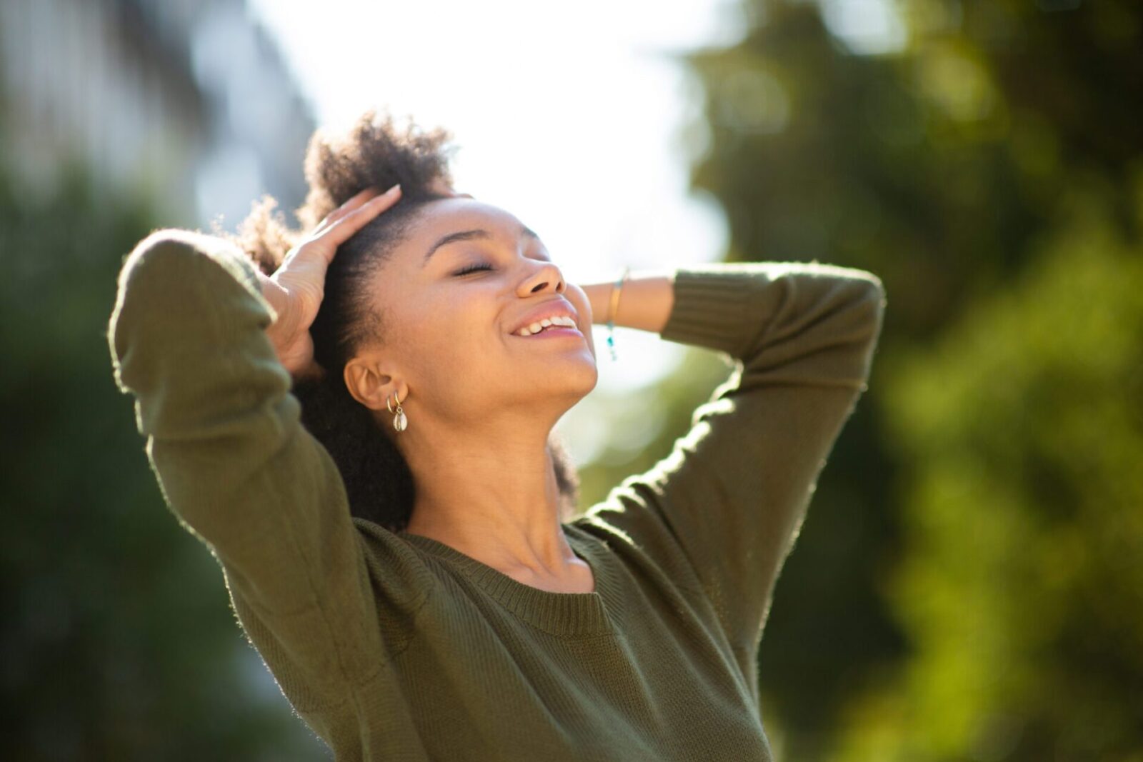 Close up carefree young black woman smiling outdoors with hand in hair A Woman in Green Dress Relaxing in Park, Wellness Designed Homes
