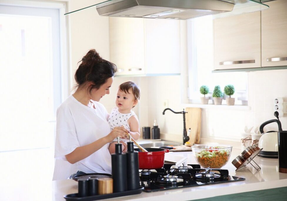 A Woman in a Modular Kitchen Cooking and Holding A Child